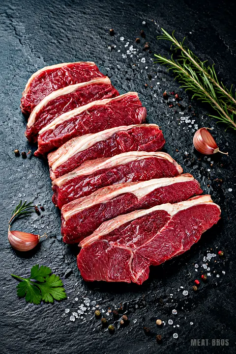 Rib eye de res porcionado en filetes gruesos, con su borde de grasa